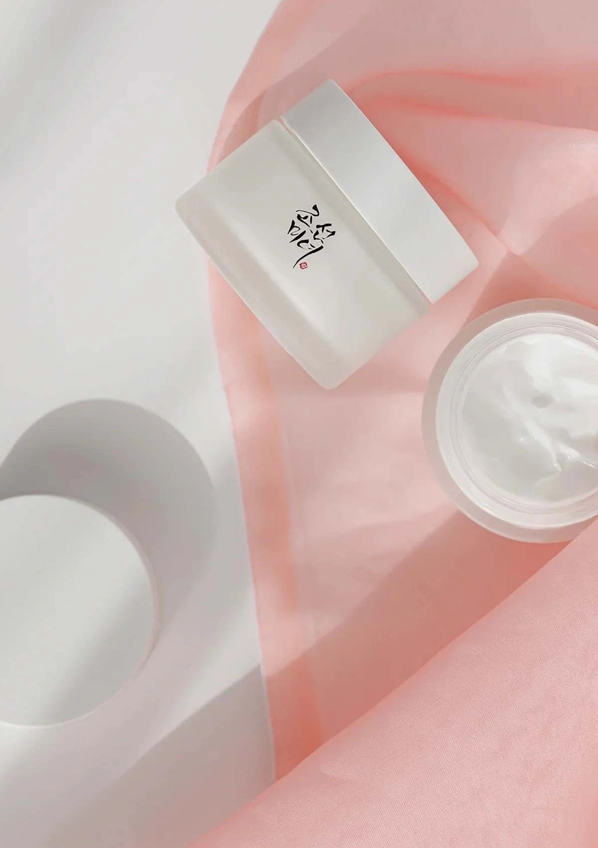 Skincare product with a jar and applicator on a soft pink background